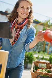 Woman with a tablet smiling selling fruits and vegetables, handing a customer their credit card